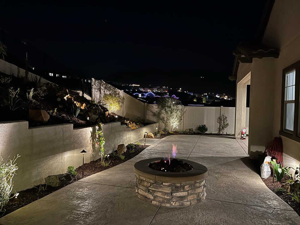 Nighttime photo of a well-lit backyard in the Terra community of Corona, CA, featuring an illuminated fire pit and landscaped outdoor space.